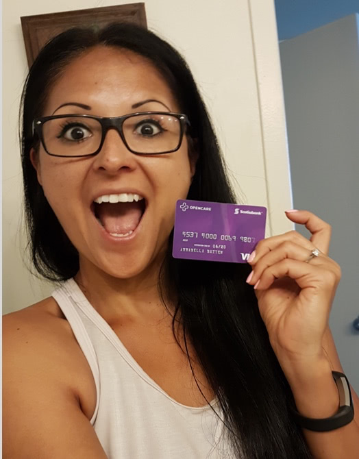 Young girl with glasses smiling enthusiastically holding an Opencare visa giftcard